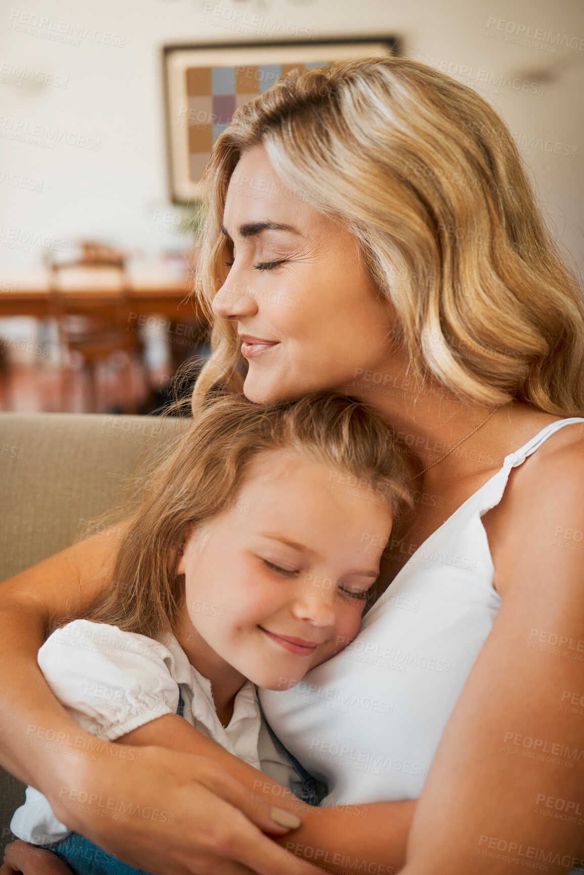 Buy stock photo Young loving caucasian mother hugging her little daughter sitting on the couch together at home. Carefree girl embracing her mom resting on the couch