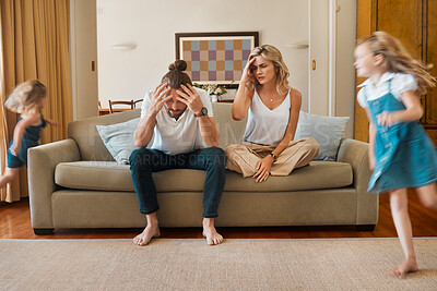 Buy stock photo Young caucasian mother and father suffering a headache with their daughters running in the lounge at home. Little sisters being playful while their parents are stressed. Woman and man upset sitting on the couch