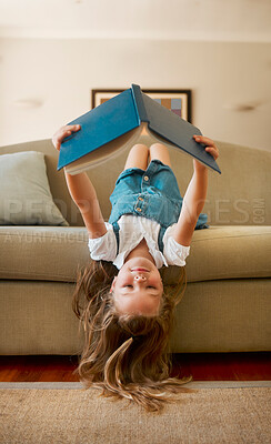 Buy stock photo Carefree content caucasian little girl reading a book alone sitting upside down on the couch at home. One cheerful positive child holding and reading a story