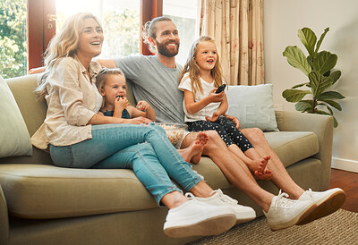 Buy stock photo Young carefree caucasian family sitting on the couch and watching a movie together in the lounge at home. Happy little sisters watching tv with their parents. Mom and dad bonding with their girls