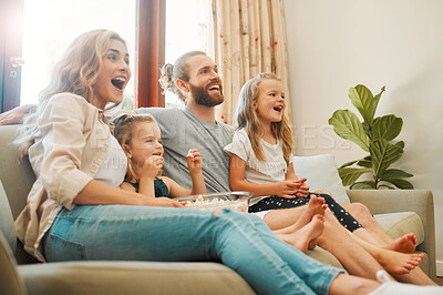Young carefree caucasian family sitting on the couch and watching a movie together in the lounge at home. Happy little siblings watching tv with their parents. Mom and dad bonding with their girls