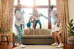 Young happy mother and father singing and dancing with their little daughters in the lounge at home. Cheerful little siblings playing guitar and having fun jumping on the couch with their mom and dad together at home