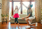 Young happy caucasian father and daughter dancing together in the lounge at home. Cheerful little girl practicing a dance with her dad. Father smiling and helping a child with a dance