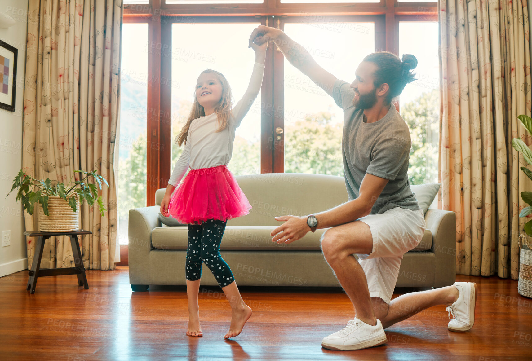 Buy stock photo Young happy caucasian father and daughter dancing together in the lounge at home. Cheerful little girl practicing a dance with her dad. Father smiling and helping a child with a dance