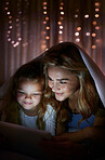 Young happy caucasian mother using a digital tablet with her little daughter in the dark before bedtime at home. Cute comfy girl watching a movie on a digital tablet with her mom