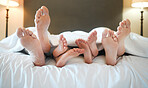 Cozy family lying in bed relaxing sleeping together. Feet and toes of parents and their tired little children sleeping taking a nap under a blanket in bed at home