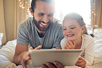 Young happy caucasian father and daughter watching videos on a digital tablet together. Cute cheerful little girl using a digital tablet with her dad while relaxing on a bed at home