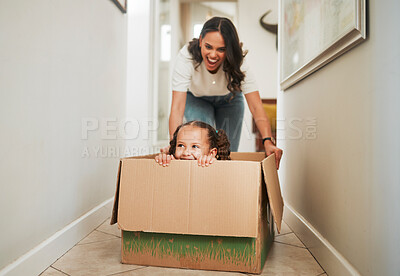 Buy stock photo Mother and daughter playing with a cardboard box. Excited little girl sitting in a box. Parent pushing her daughter in a box. Parent having fun with her child at home. Cheerful mother and daughter