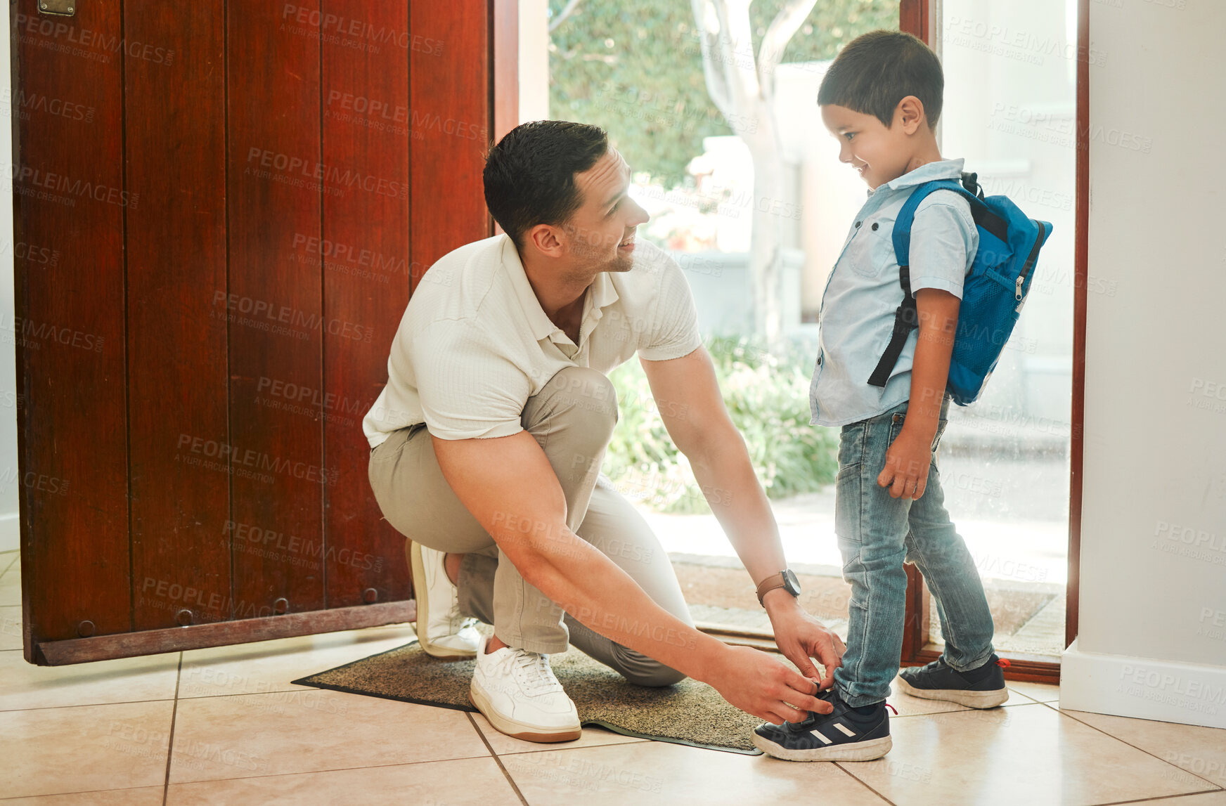 Buy stock photo Happy single father tying his son's shoelaces before school in the morning. Adorable mixed race little boy carrying a backpack and getting help from his single parent. Hispanic man and child at home