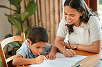 Mixed race boy learning and studying in homeschool with mom. Woman helping son with homework and assignments at home. Loving parent teaching child to draw, read and write at home in lockdown