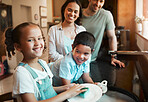 Young happy mixed race parents washing the dishes with their son and daughter in the kitchen at home. Little brother and sister helping their mom and dad clean the dishes. Girl washing a plate