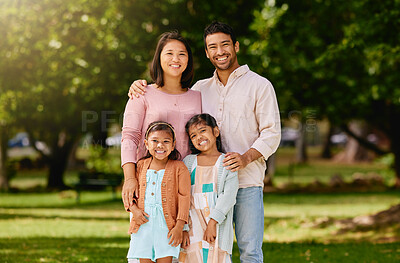 Buy stock photo Portrait of a happy mixed race family standing together in a public park on a sunny day. Asian parents and two little daughters enjoying a day outdoors