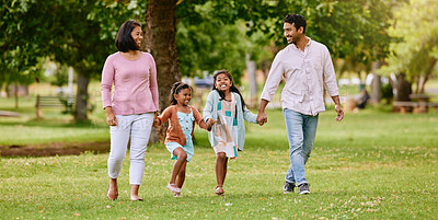 Young happy mixed race family holding hands and walking together in a park. Loving parents spending time with their little daughters in nature. Sisters bonding with their mom and dad outside
