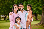 Portrait of happy asian family standing close together in a park. Adorable little girls enjoying free time with their mother and father on a weekend outside. Smiling couple embracing their daughters