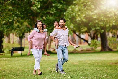 Buy stock photo Mixed race family in the park. Happy young mother and father piggybacking their son and daughter outside. Couple carrying their kids while walking on grass during. Two sisters on parents' backs