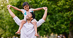 Happy mixed race father and cute playful daughter having fun at the park outdoors with copyspace. Carefree man carrying cheerful girl on shoulders for piggyback ride. Parent bonding with kid 