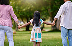 Rear view of parents and little girl holding hands while walking outdoors in park on a sunny day. Loving and caring family with one child bonding and having fun outdoors