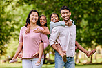 Portrait of happy asian family standing close together in a park. Adorable little girls enjoying free time with their mother and father on a weekend outside. Smiling mixed race couple embracing their daughters