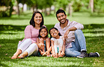 Young happy mixed race family relaxing and sitting on grass together in a park. Loving hispanic parents spending time with their little daughters in nature. Girls bonding with mom and dad outside