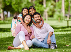 Portrait of happy asian family in the park. Adorable little girls bonding and hugging their parents outside in a park. Full length husband and wife sitting and enjoying free time with their daughters