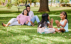 A happy asian couple lying together on grass outside, loving parents enjoy quality time with their little daughters playing a game. Couple bonding during family time at park with adopted foster sister