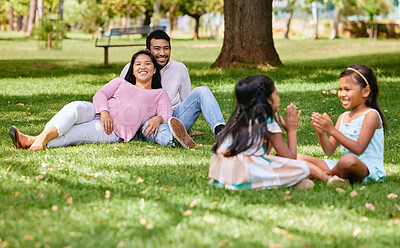 Buy stock photo A happy asian couple lying together on grass outside, loving parents enjoy quality time with their little daughters playing a game. Couple bonding during family time at park with adopted foster sister