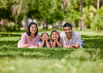 Young happy mixed race family relaxing and lying on grass together in a park. Loving parents spending time with their little daughters in nature. Joyful girls bonding with mom and dad outside