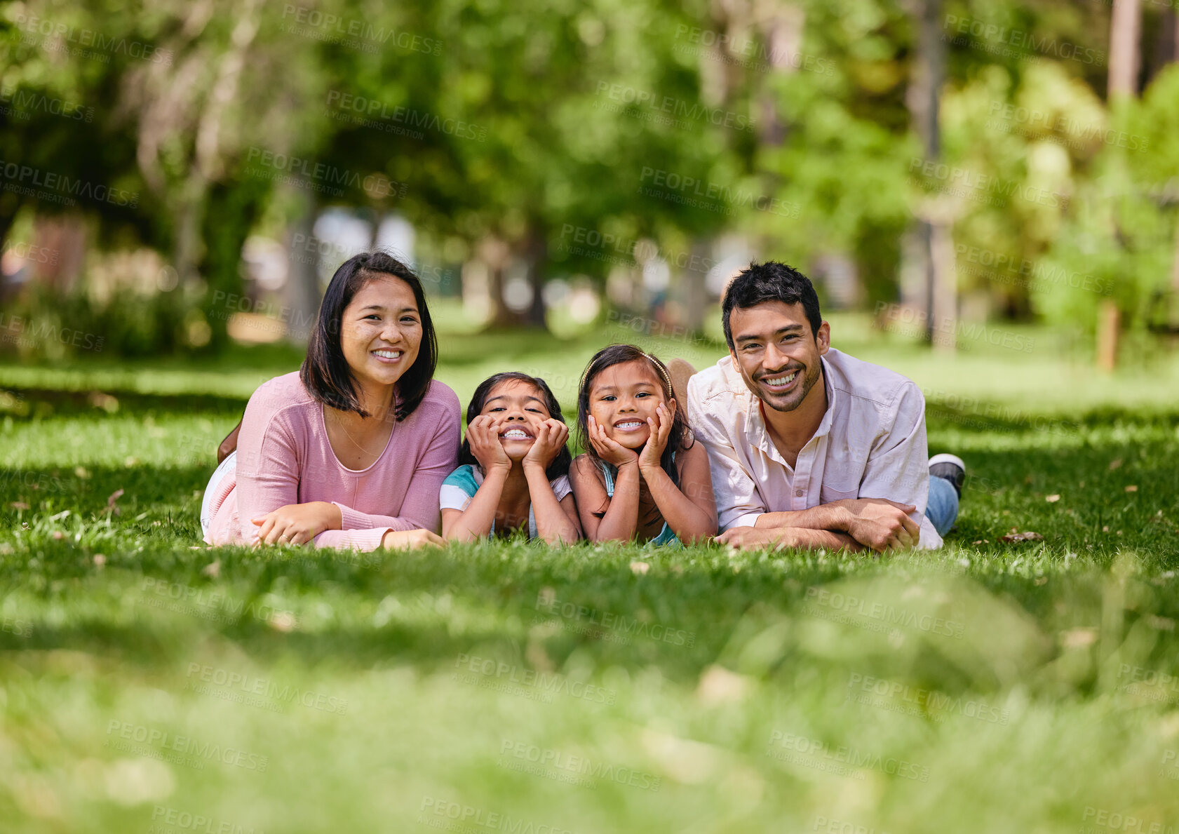 Buy stock photo Young happy mixed race family relaxing and lying on grass together in a park. Loving parents spending time with their little daughters in nature. Joyful girls bonding with mom and dad outside
