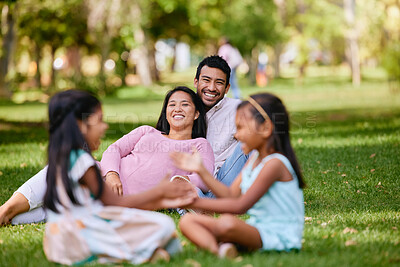 Buy stock photo Portrait of happy asian couple laughing while lying together on grass. Loving parents spending time together with their little daughters playing close. Couple bonding during family time at park