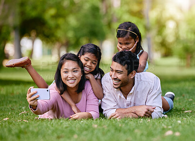 Buy stock photo Multiracial family taking selfies in the park. Happy family bonding in the park. Little girls relaxing with their parents in a garden. Mother using a cellphone to take photos with her family. 