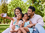 Happy asian family taking selfies and video call while relaxing at the park. Loving parents capturing photos and pictures for special childhood memories while bonding with carefree smiling daughters
