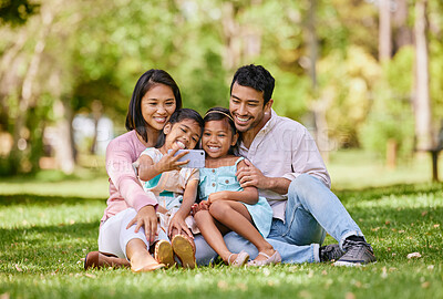 Buy stock photo Happy asian family taking selfies on a cellphone in a park. Adorable little girls bonding with their parents outside. Full length husband and wife sitting and enjoying free time with their daughters