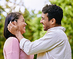 Loving husband putting hair behind wife's ear standing face to face in a park. Happy romantic moments of lovely couple spending time together outdoors. Man caressing woman's face