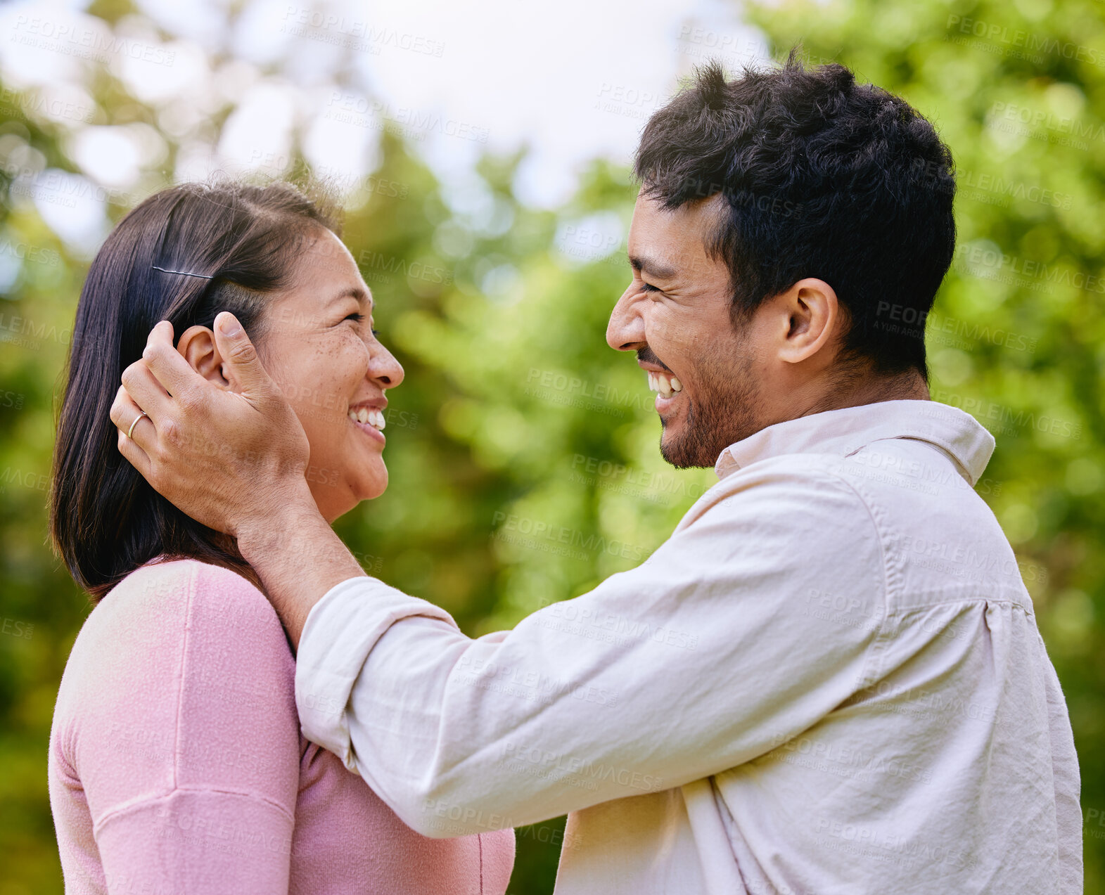 Buy stock photo Loving husband putting hair behind wife's ear standing face to face in a park. Happy romantic moments of lovely couple spending time together outdoors. Man caressing woman's face