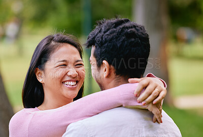 Happy Asian couple looking in love while standing face to face in a park. Happy romantic moments of lovely couple spending time together outdoors. Wife putting hands around husband
