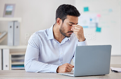 Young mixed race businessman suffering from a headache working on a laptop in an office alone at work. One hispanic man dealing with a problem while working. Male boss feeling tired sitting at a desk