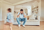 Young caucasian father suffering from a headache while his son runs in the lounge at home. Carefree boy running in the living room while his dad looks tired. Man looking upset while his child plays