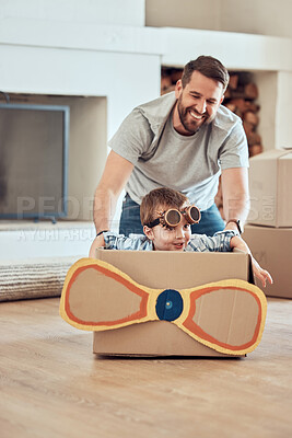 Buy stock photo Happy single father pushing his little kid in homemade aeroplane cardboard box at home. Adorable little boy sitting in makeshift plane and playing with single parent in a living room in their new home