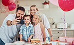 Happy caucasian family celebrating a birthday at home. Parents smiling for selfie or video call with two kids while having a party at home with balloons and cake