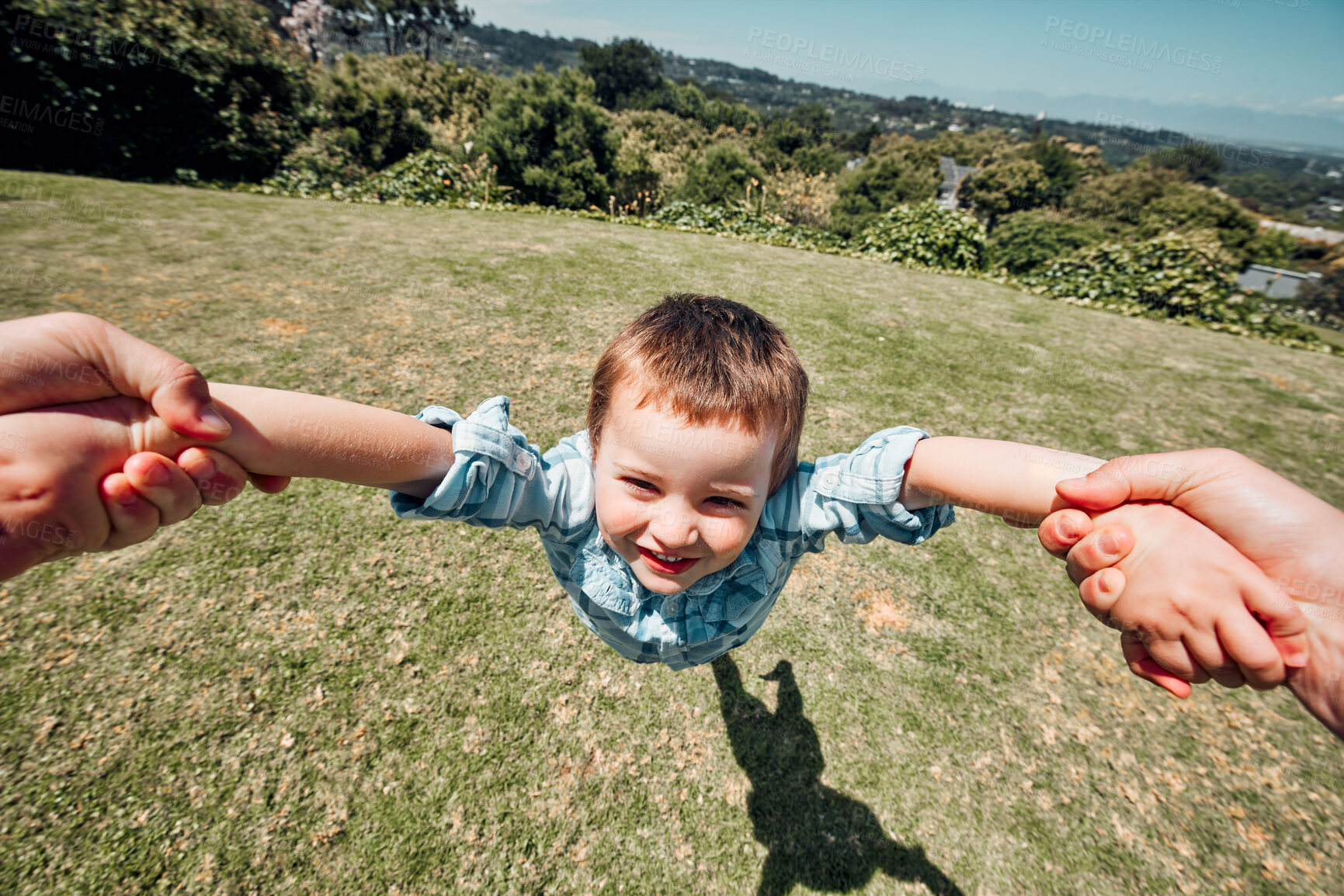Buy stock photo Closeup portrait of little boy being swung around by parent outside in nature. POV shot of a little boy pretending to fly and having fun while father spinning him around by the arms on a sunny day