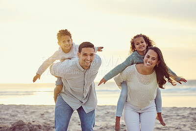 Buy stock photo Portrait of a happy mixed race family standing and having fun together on the beach. Parents giving their children a piggypack while on holiday. Little siblings playing with their parents on vacation