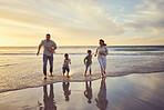 Family on holiday running on the beach. Family having fun in the ocean at sunset. Happy family running in the water at the beach. Hispanic family on vacation together. Parents running with children 