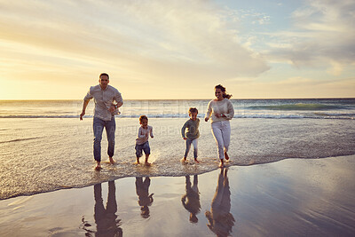 Family on holiday running on the beach. Family having fun in the ocean at sunset. Happy family running in the water at the beach. Hispanic family on vacation together. Parents running with children