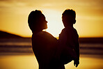 Silhouette shot of a mother holding her son on the beach at sunset. Woman and kid spending time together at the beach against golden sky. Mom and son sharing a beautiful bond