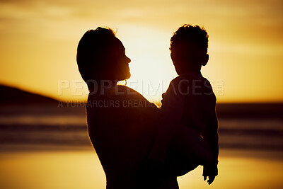 Silhouette shot of a mother holding her son on the beach at sunset. Woman and kid spending time together at the beach against golden sky. Mom and son sharing a beautiful bond