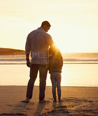 Buy stock photo Rear view shot of father and daughter spending time together at the beach at sunset. Loving father embracing little girl while standing together by the sea