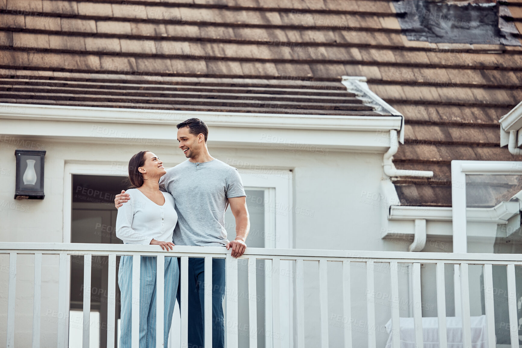 Buy stock photo Happy young mixed race couple standing on the balcony at their new home. Hispanic couple looking into each others eyes. Loving husband and wife standing outside getting fresh air