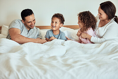 Buy stock photo Mixed race family lying in bed, smiling and playing. Latino parents having fun with their little cute kids. Brother and sister in bed with their mother and father at home in the morning
