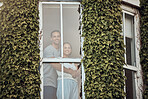 Happy young mixed race couple standing in their window. Loving couple bonding and spending time together at home.  Lovers standing by a window with leaves growing up the exterior wall. Warm and cozy at home 