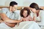 Playful parents tickling their little daughter while lying in bed together. Cheerful couple bonding with their adorable little girl at home in the morning. Cute little girl laughing while playing with mom and dad. Waking up happy